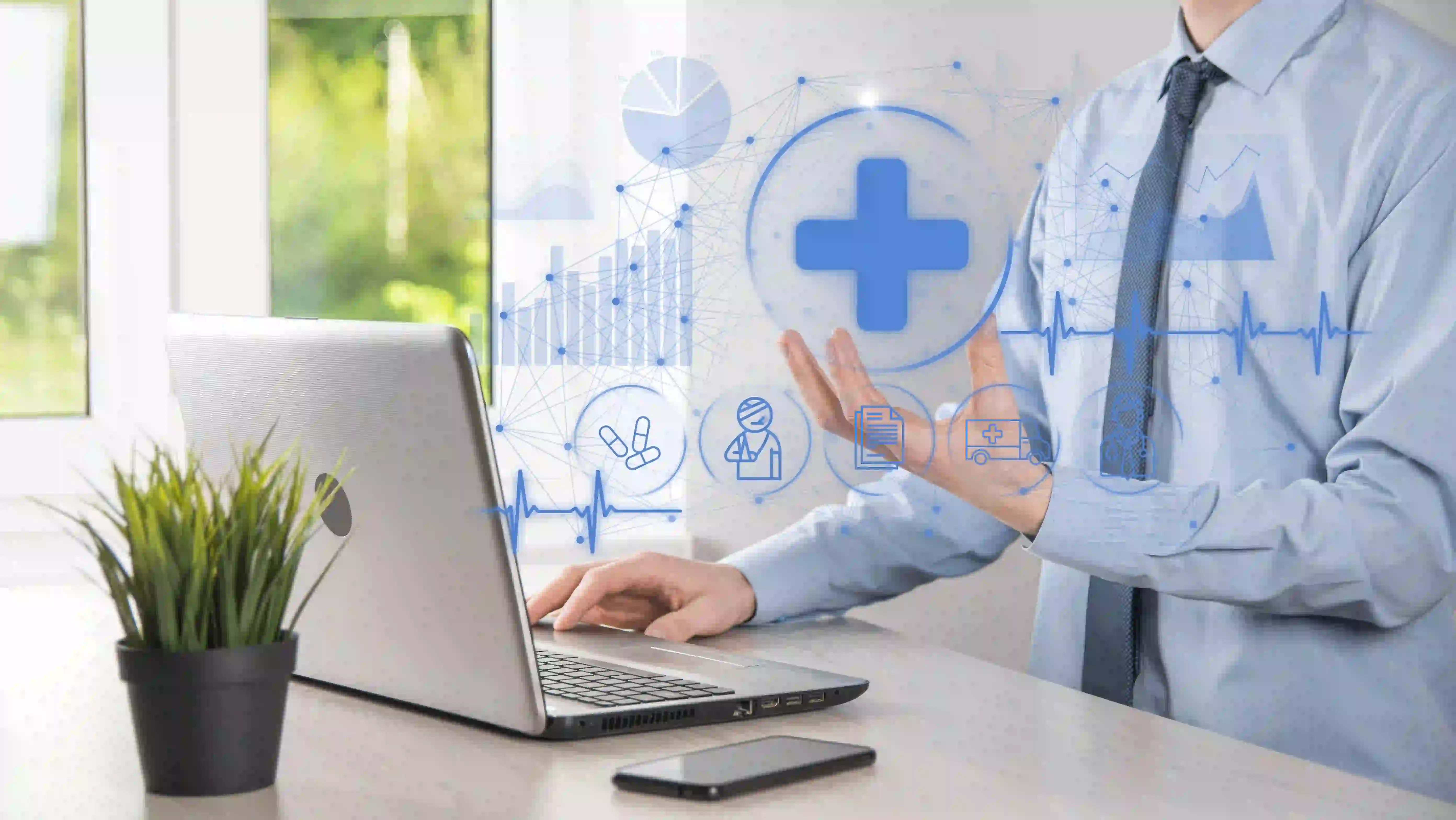 A person in a light blue shirt and tie is using a laptop on a desk with a potted plant and a smartphone. The image features overlaid graphics of medical icons, including a blue cross, pills, and other healthcare-related symbols, indicating an electronic health record system concept